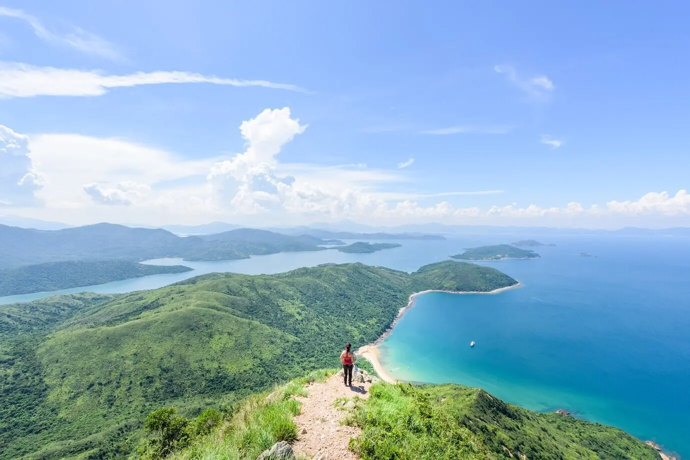A beautiful shot of a woman standing against a backdrop of forested hills and a blue ocean.