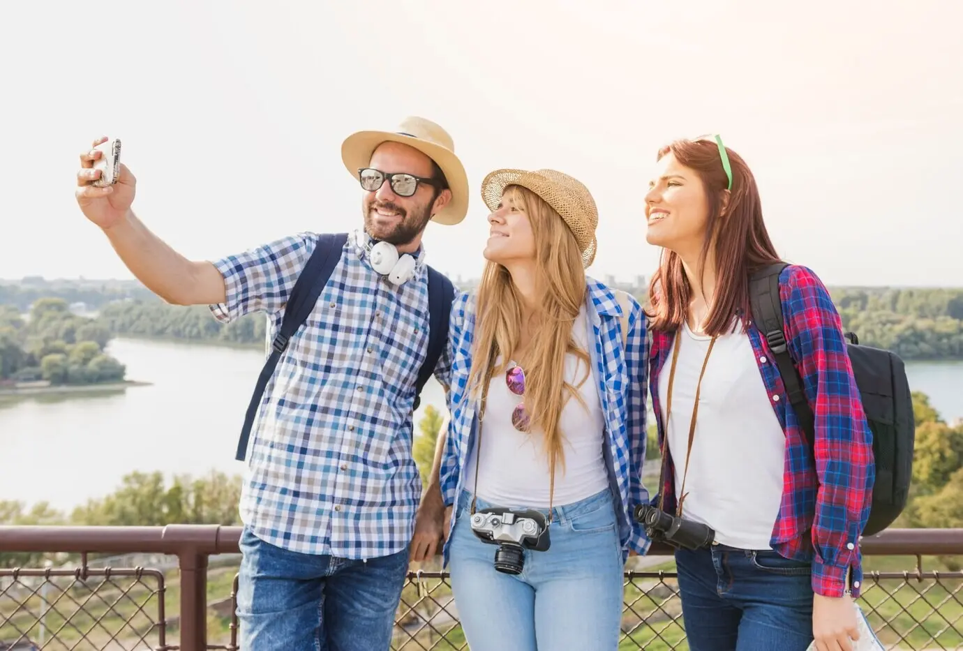 A group of happy friends taking a selfie with a cellphone outdoors.